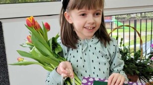 dziewczynka z prezentem od kolegów z grupy z okazji dnia kobiet - bukietem kwiatów i laurką