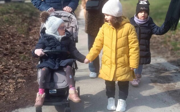 dwie dziewczynki (jedna na wózku inwalidzkim) spacerują, trzymając się za ręce